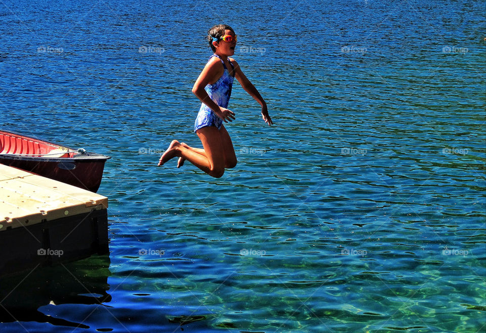 Girl jumping off dock into a lake in summer vacation