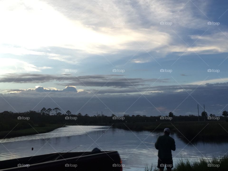 Man fishing in Florida's intercoastal and river with sunset and water reflection.