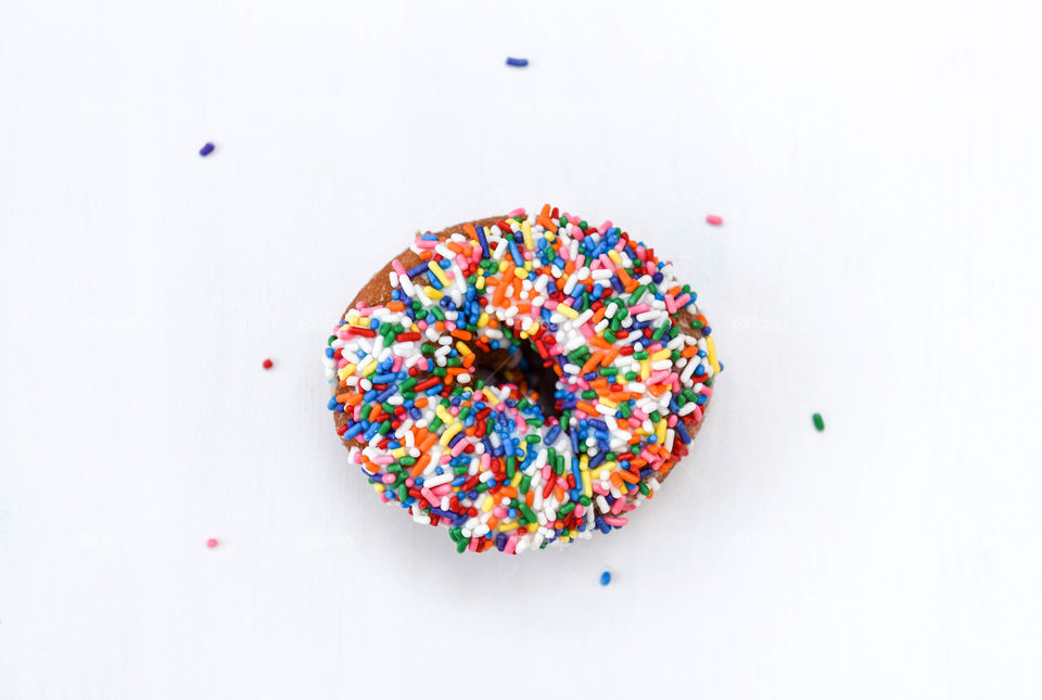 Flat lay of a rainbow sprinkles donut on a white table