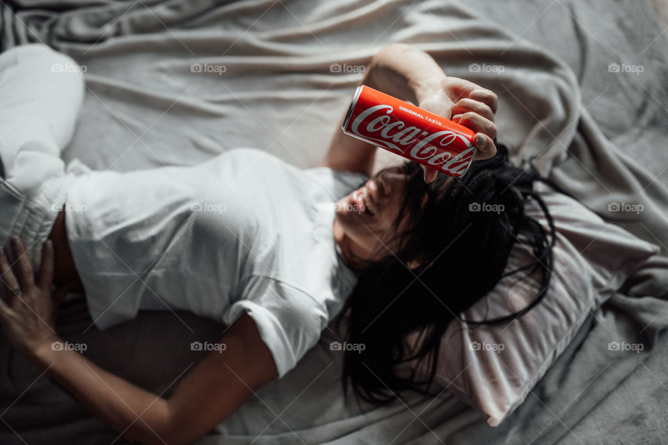 the girl lies on the bed and holds a Coca Cola