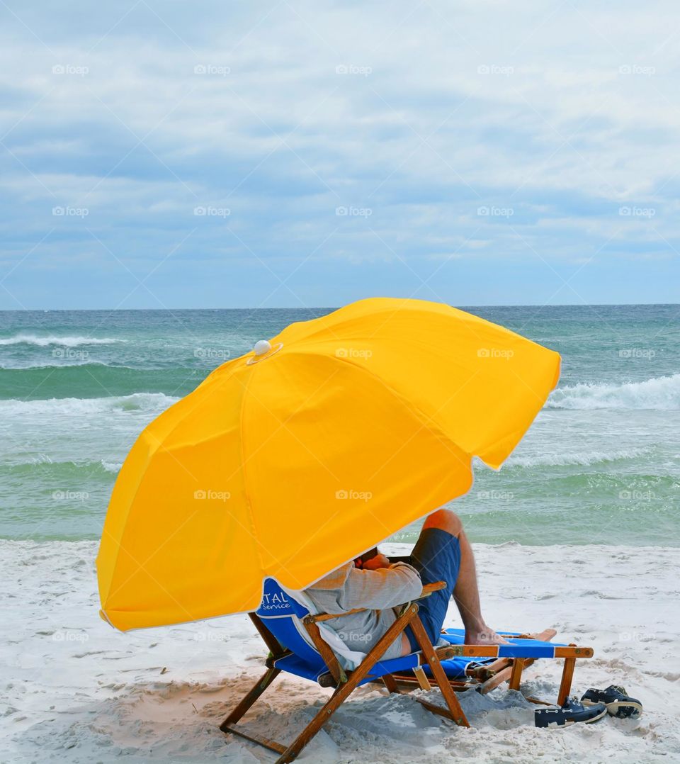 Chilling on the beach under his yellow umbrella in front of the Gulf of Mexico - Yellow is a color associated with sun