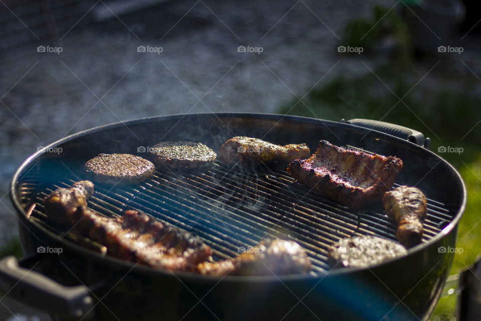 A portrait of a barbecue grill with some different kinds of meat on it. the meat is at the side because it can grill some more without burning.