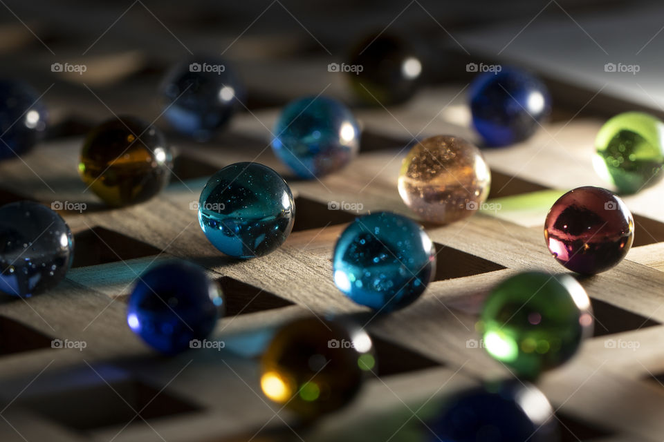 A colorful portrait of rows of colored marbles shining their color on to the wooden surface.