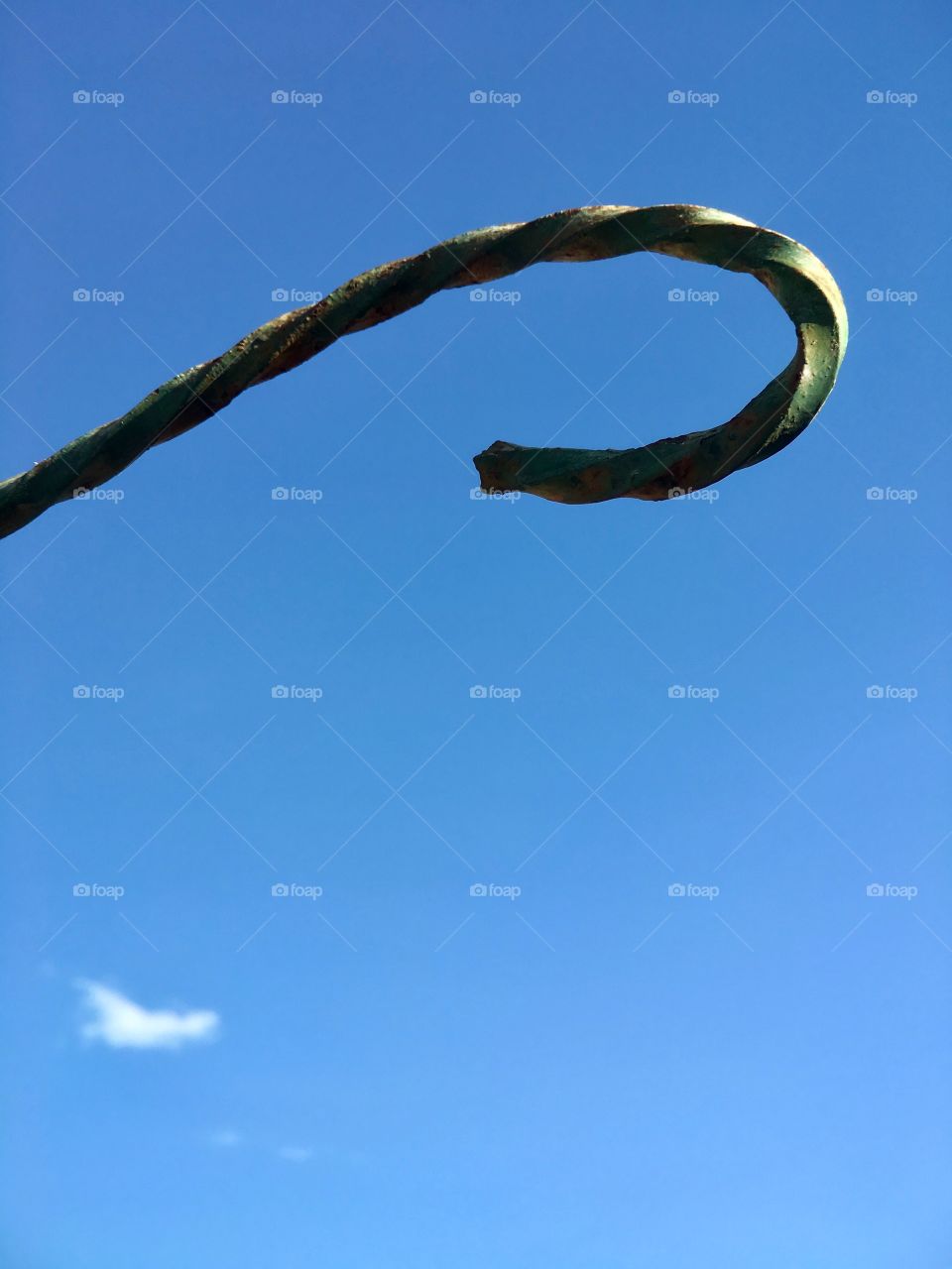 Curved wrought iron rod jutting out against vivid blue sky minimalist 