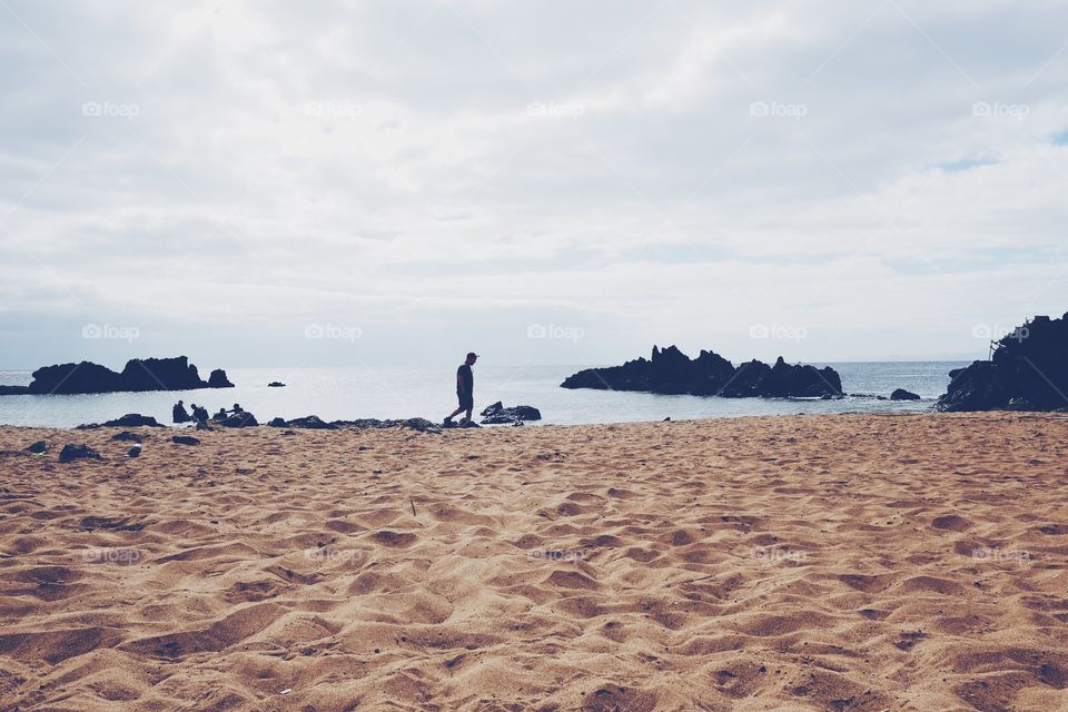 Man walking on a sandy beach alone near the water