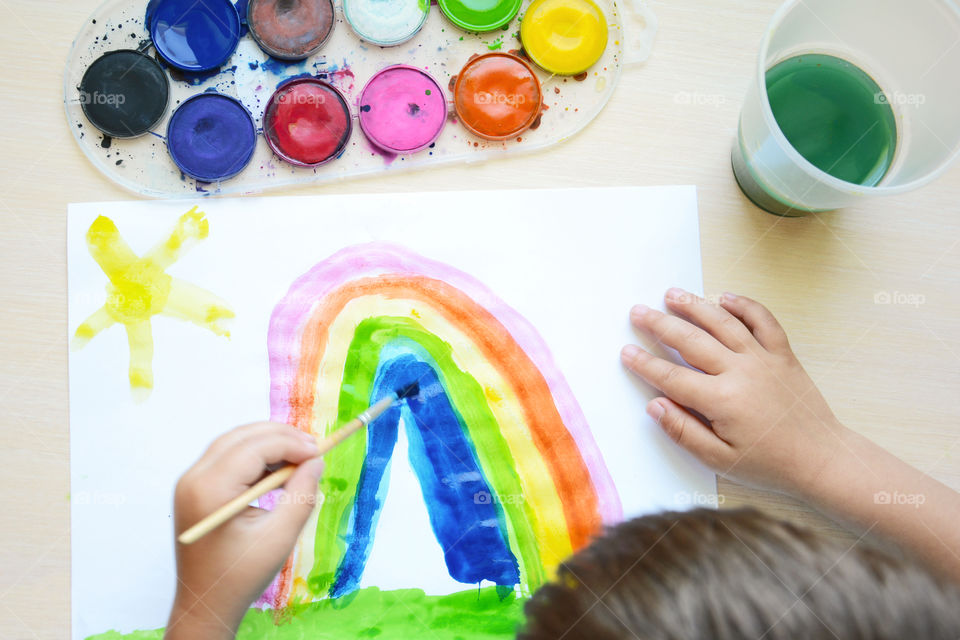 A little boy drawing rainbow with watercolor