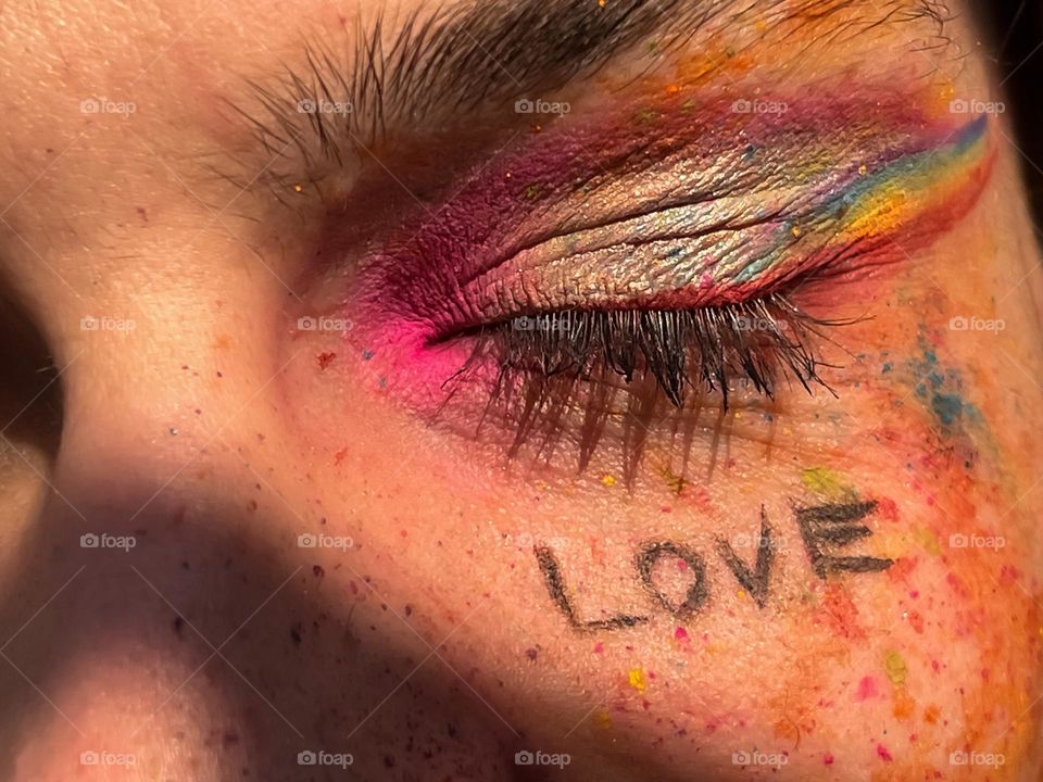 Close up of a man’s closed eye with pride colours and freckles 