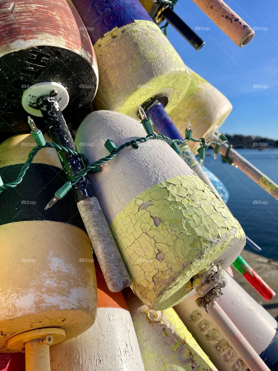 A close up of a stack of lobster buoys show the aged and weathered look to the paint.