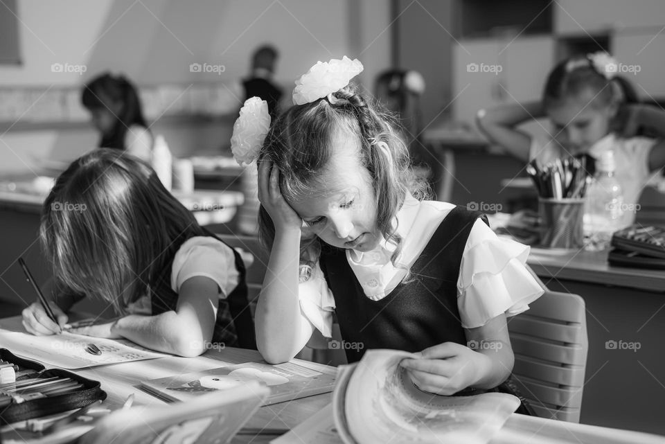 black and white photo girl first grade sitting at her desk at school sad