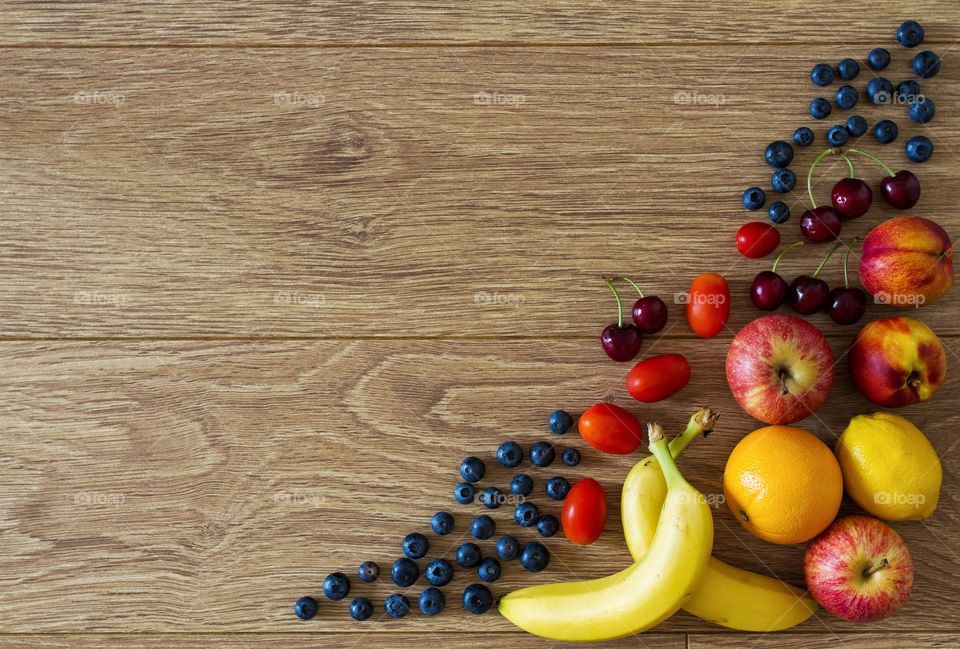 A variety of different fruits and berries on a wooden table forming a frame in the corner of the image. A food background.