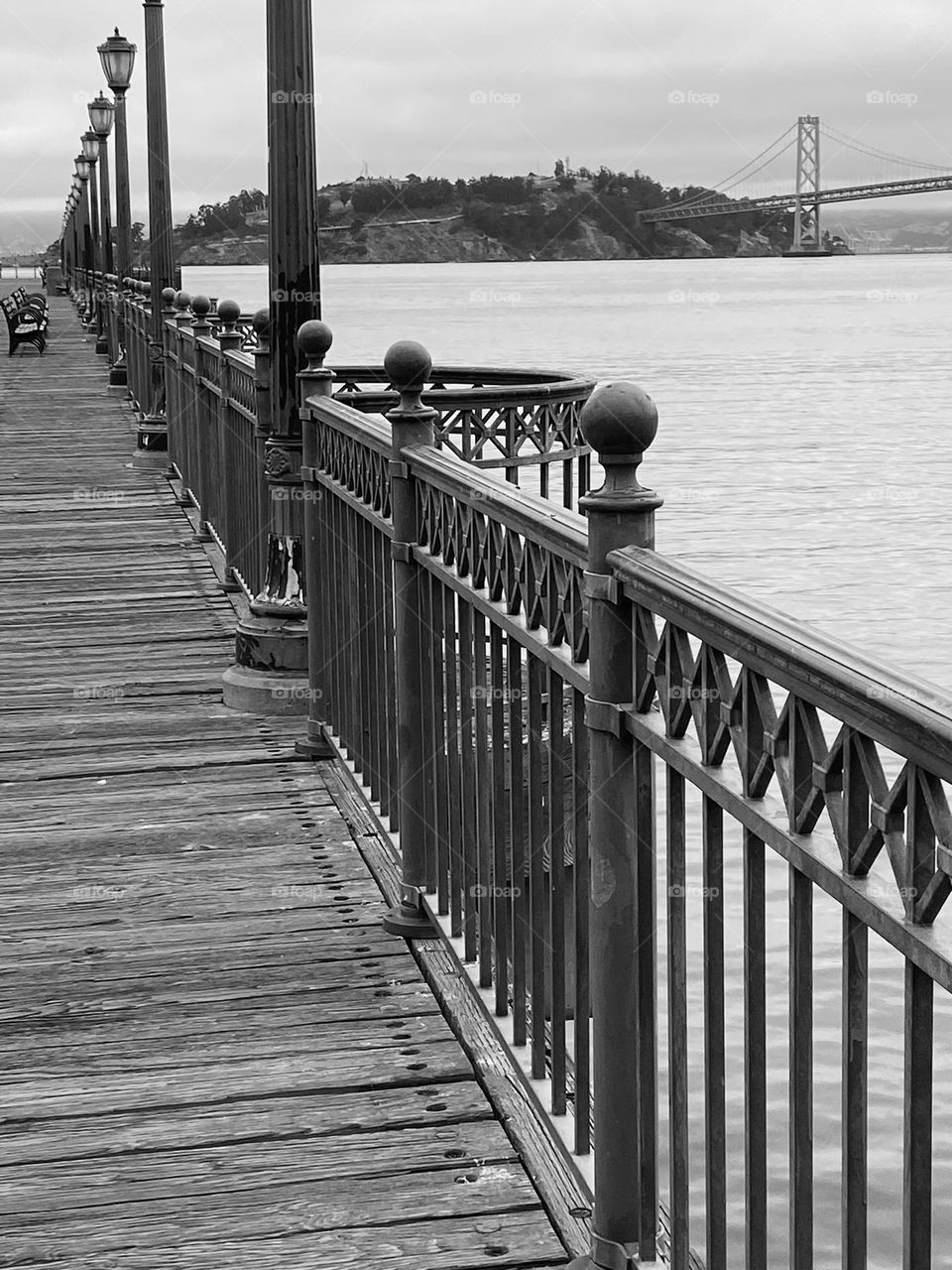 Black and white photo of a wooden pier with the Golden Gate Bridge in the background.