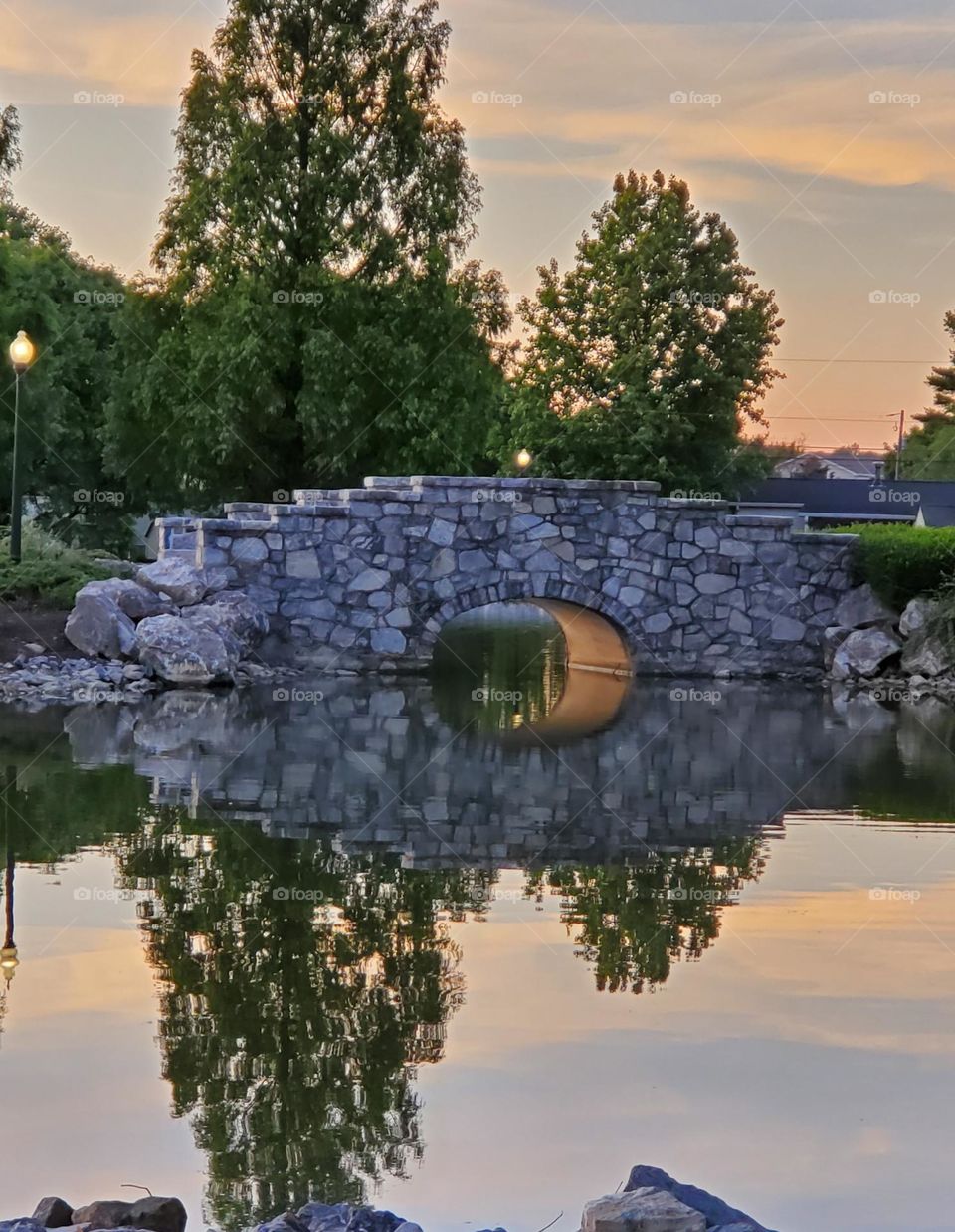 A beautiful stone bridge creates a mirror reflection on a still pond as evening falls. 