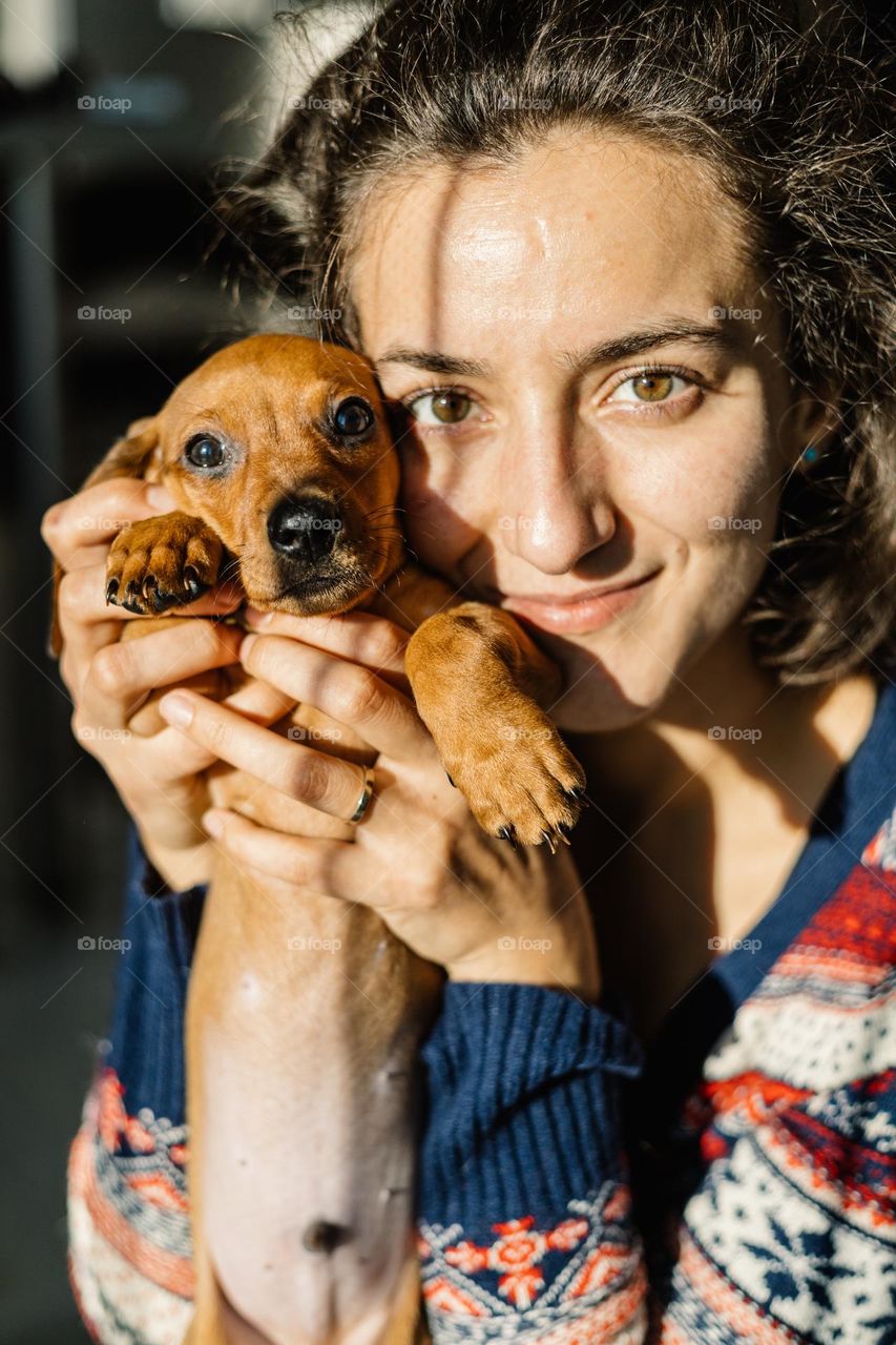 Young woman being happy with her little puppy, while at home on a winter sunny afternoon.