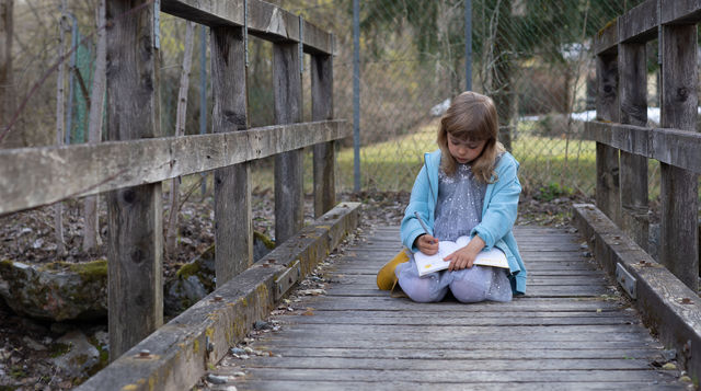 Girl of 6 years is learning her HappySelf journal on a wooden bridge in the village she lives.