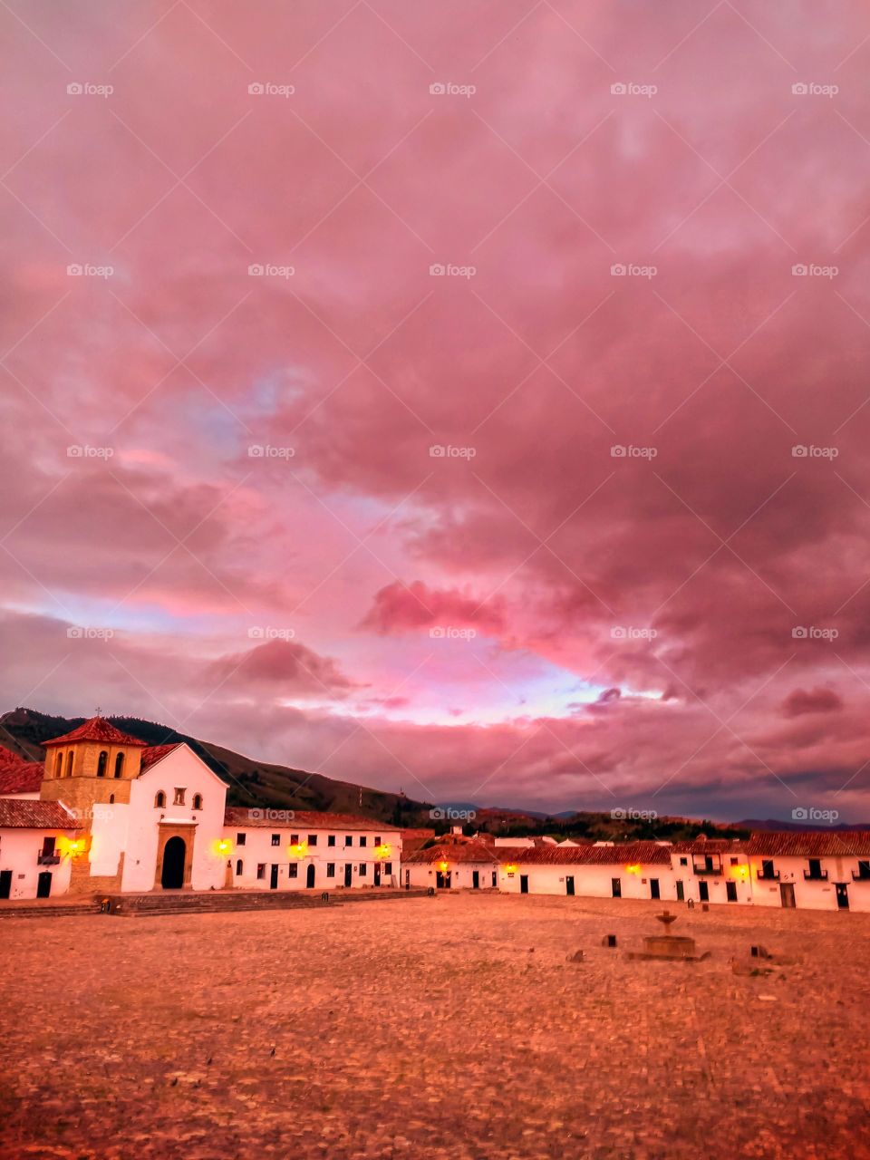 Amanecer de nubes rosadas en la plaza principal de Villa de Leyva Boyacá Colombia Sur America. Sunrise of pink clouds in the main square of Villa de Leyva. Beautiful destination, vibrant color landscape vertical ligths Sunrise