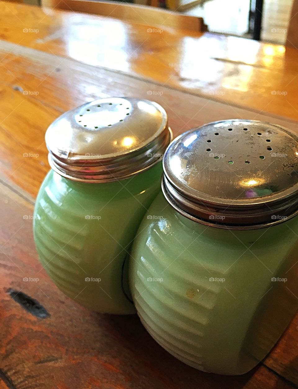 Shake it up!  Salt and pepper shakers - green ceramic with shiny silver tops sitting on a wood tabletop. 