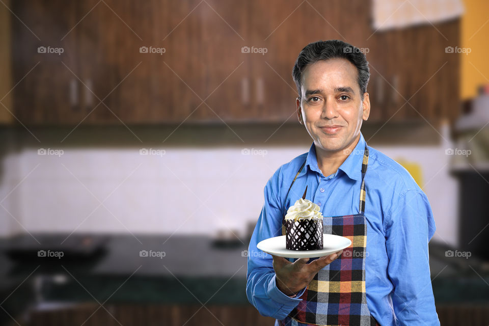 Indian man in kitchen interiors with a chocolate cake
