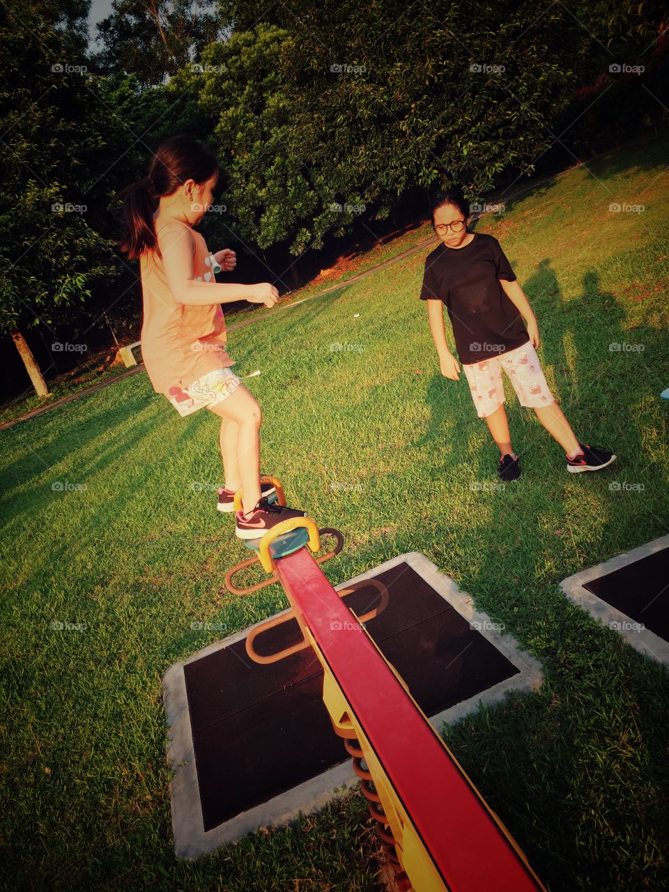 Two girls at age 8 and 10 playing sea-saw at the park.