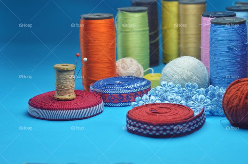 a beautiful banner with ribbons and ruffles next to a wooden spool of thread and large colored spools in the background. theme of sewing and needlework