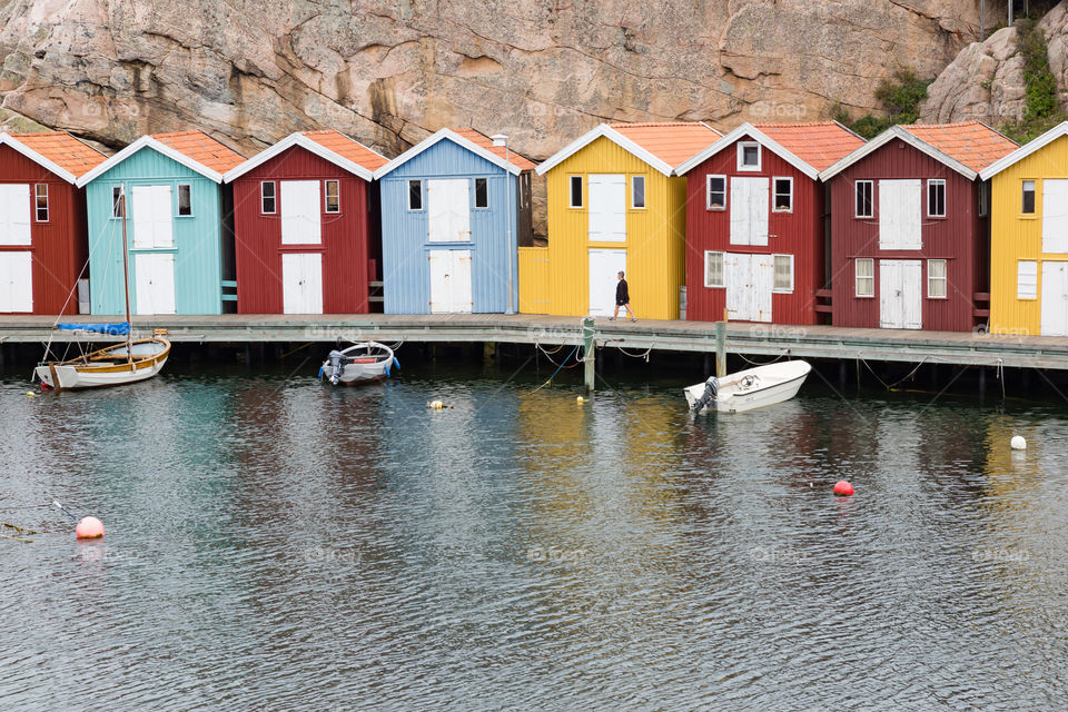 Woman walking on wooden pier surrounded by colorful boathouses 