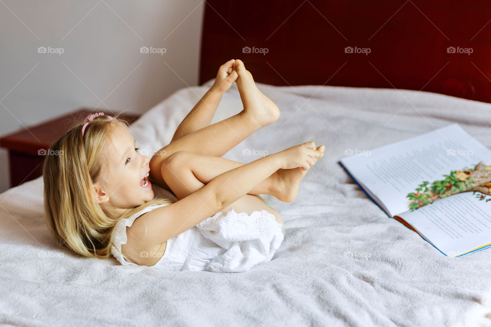 Happy little girl with blonde hair lying in bed