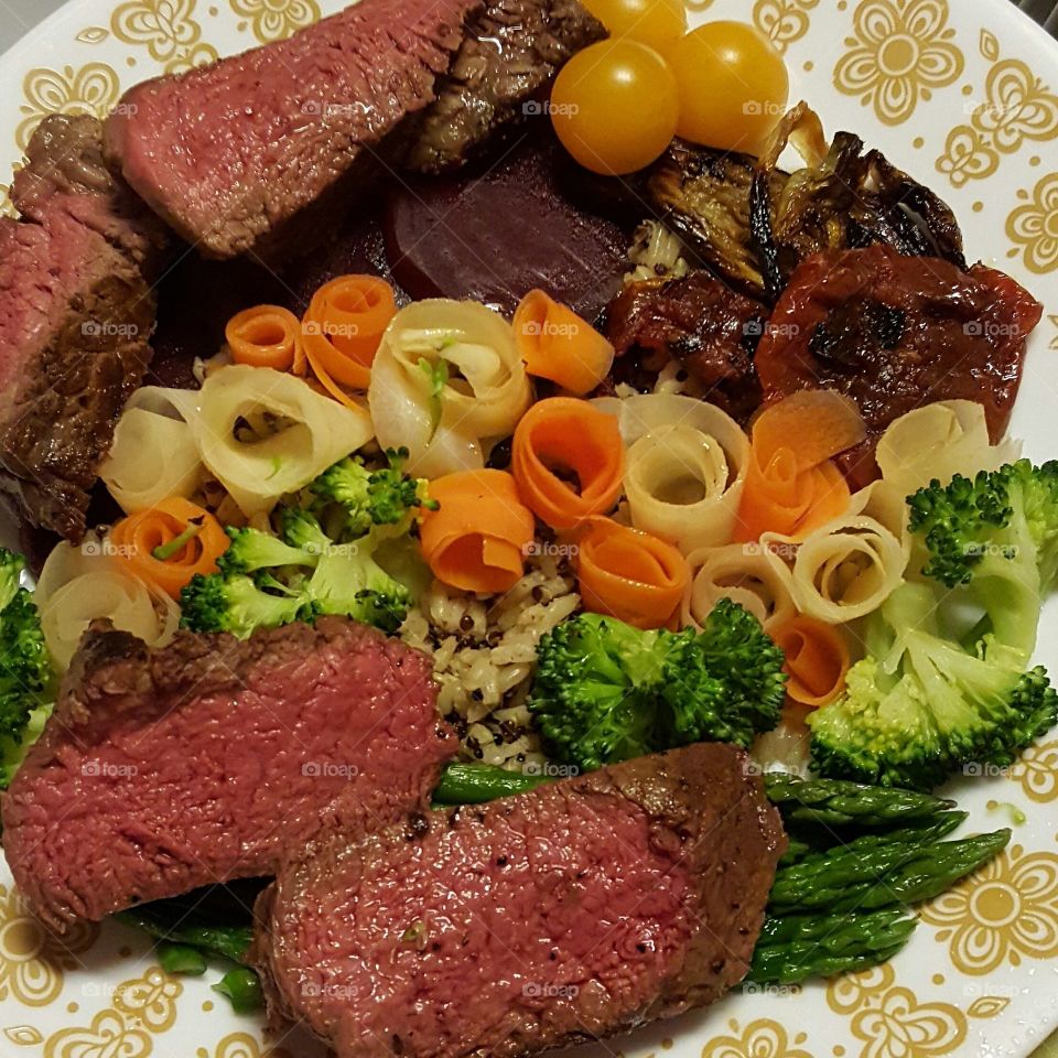 Beef tenderloin slices with broccoli, asparagus, yellow tomatoes, oven roasted fennel and beefsteak tomato slices, steamed white and yellow carrot flowers, drizzled with butter, on a bed of herb and garlic quinoa and brown rice.