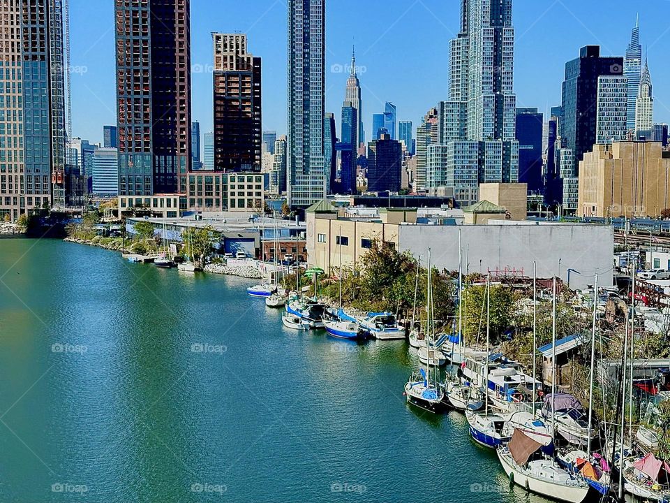 This is picturesque “Newtown Creek” seen from the “Pulaski Bridge” in LIC, Queens with all its boats and fantastic views of the “Big Apple” NYC reaching all the way to “Manhattan” including the “Empire State Building”. 2023. Hypnotic Productions