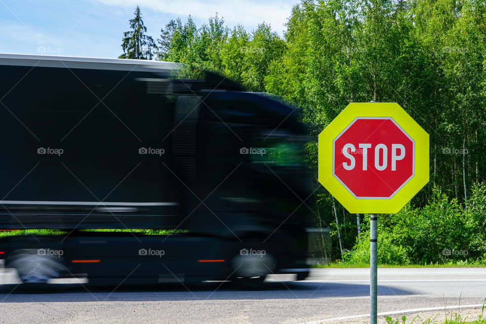 red stop road sign with yellow octagonal frame in the foreground and blurred fast truck in the background
