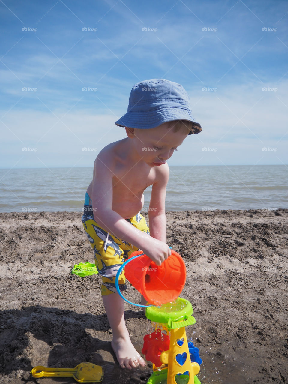 Toddler boy pouring water into his beach toy.