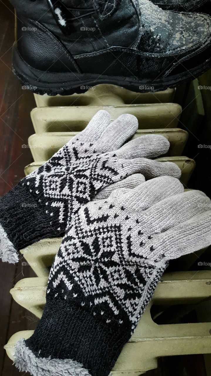 Winter gloves and boots set on an old cast iron radiator to dry after a day of fun in the snow.