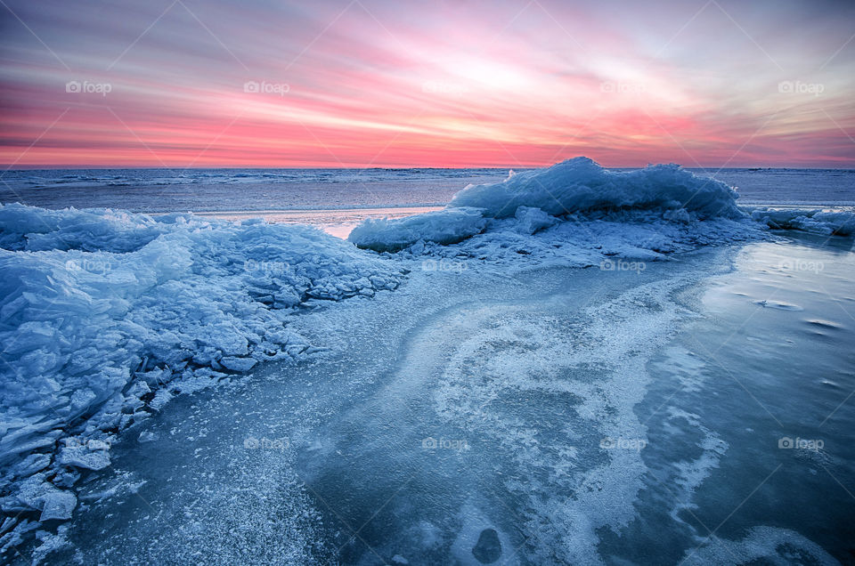 Frozen winter sunrise seascape with ice and colorful sky.