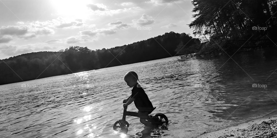 A toddler boy rides his bike into the lake water. silhouette. relection