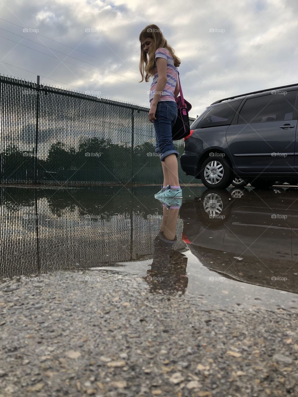 Girl stands in puddle with urban fence and minivan in background