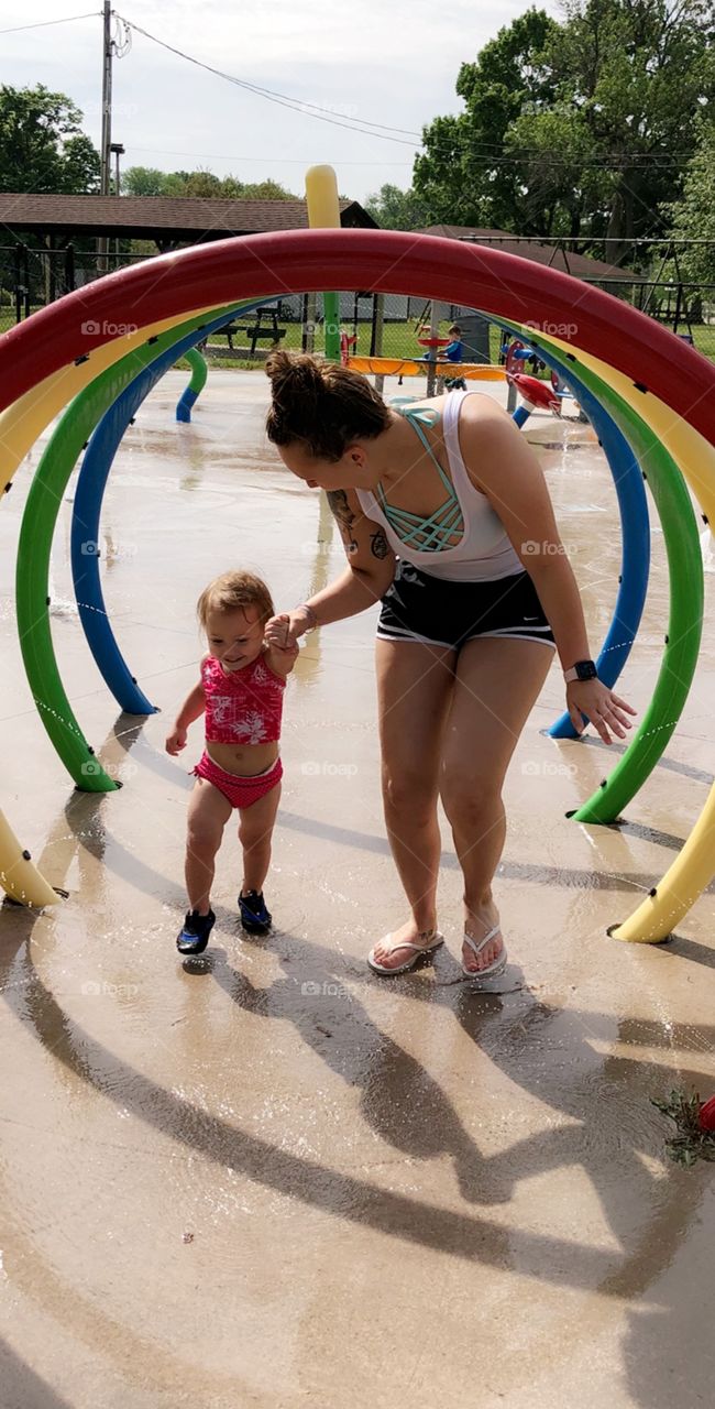 Toddler girl and young woman running through water at water park