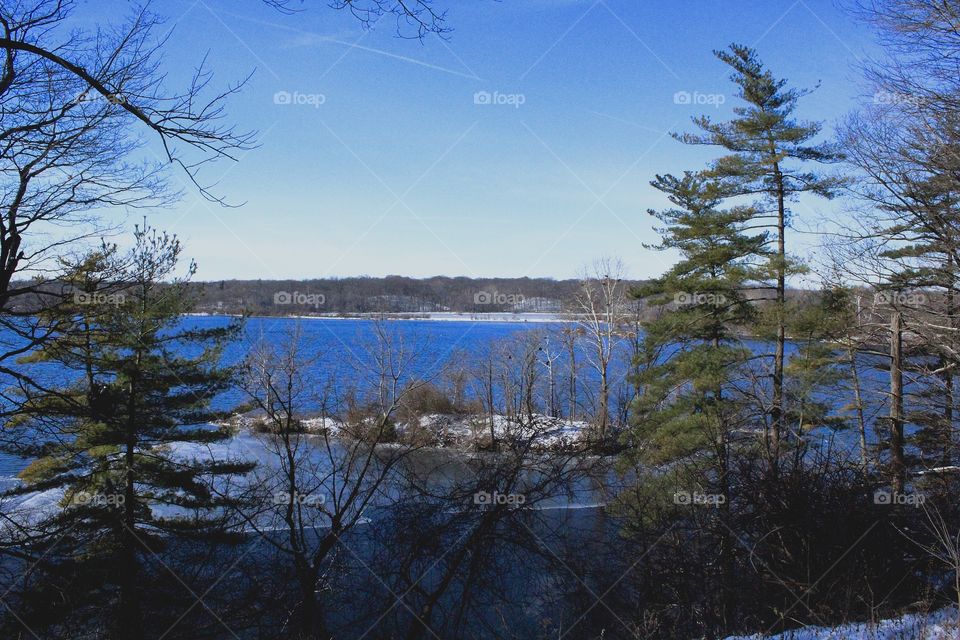 Gorgeous winter scene with green pine trees and stunning, clear blue water after a recent snowfall with some ice forming on a scenic lake 