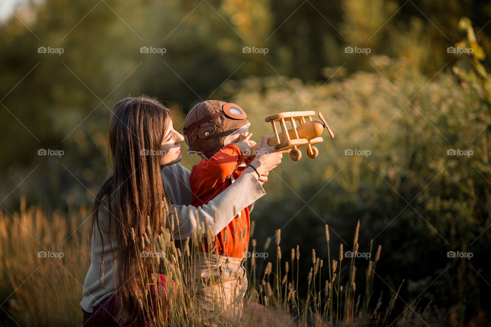 Mother with son playing with wooden plane at sunset