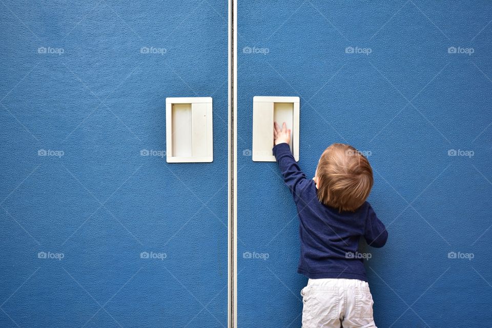Cute curious toddler boy trying to open door