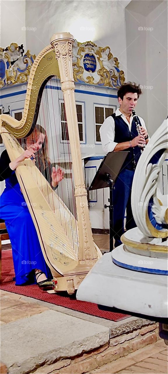 A lady plays the harp accompanied by a gentleman playing the clarinet at the “Inselkirche”, the “Island Church” on the island “Hiddensee” in the “Baltic Sea” or “Ostsee” in “Mecklenburg - Western Pomerania”, Germany. 2024. Hypnotic Productions