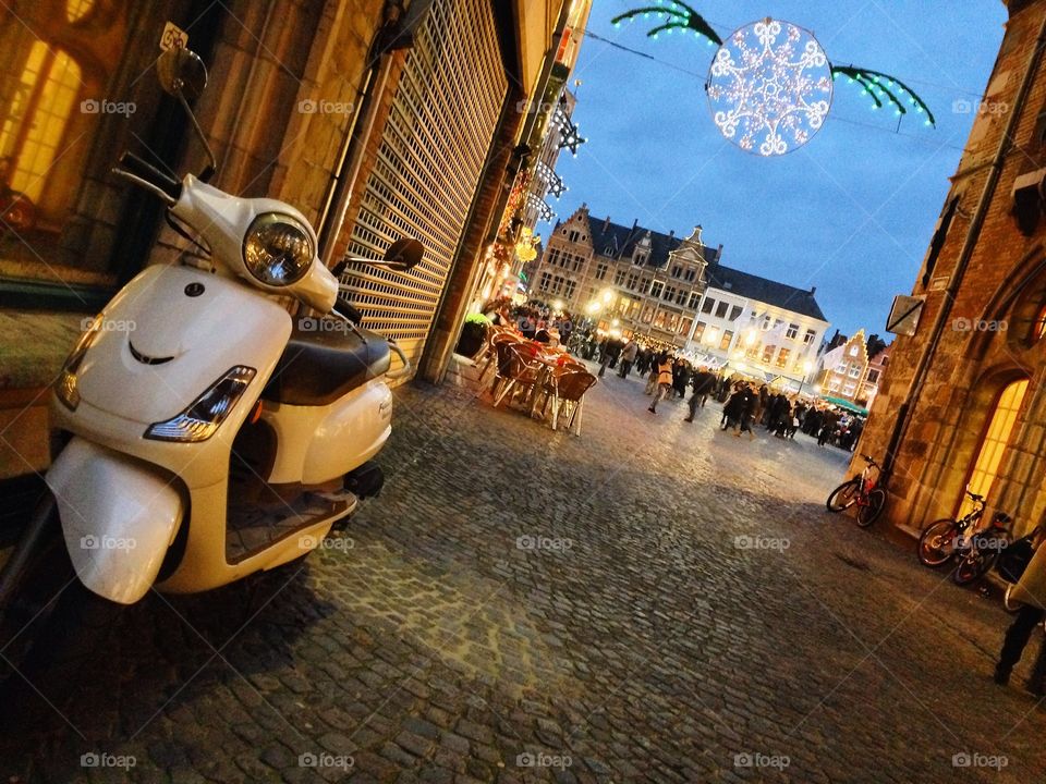 A lone scooter awaits its riders in an empty yet festive road in Brugge, Belgium. 