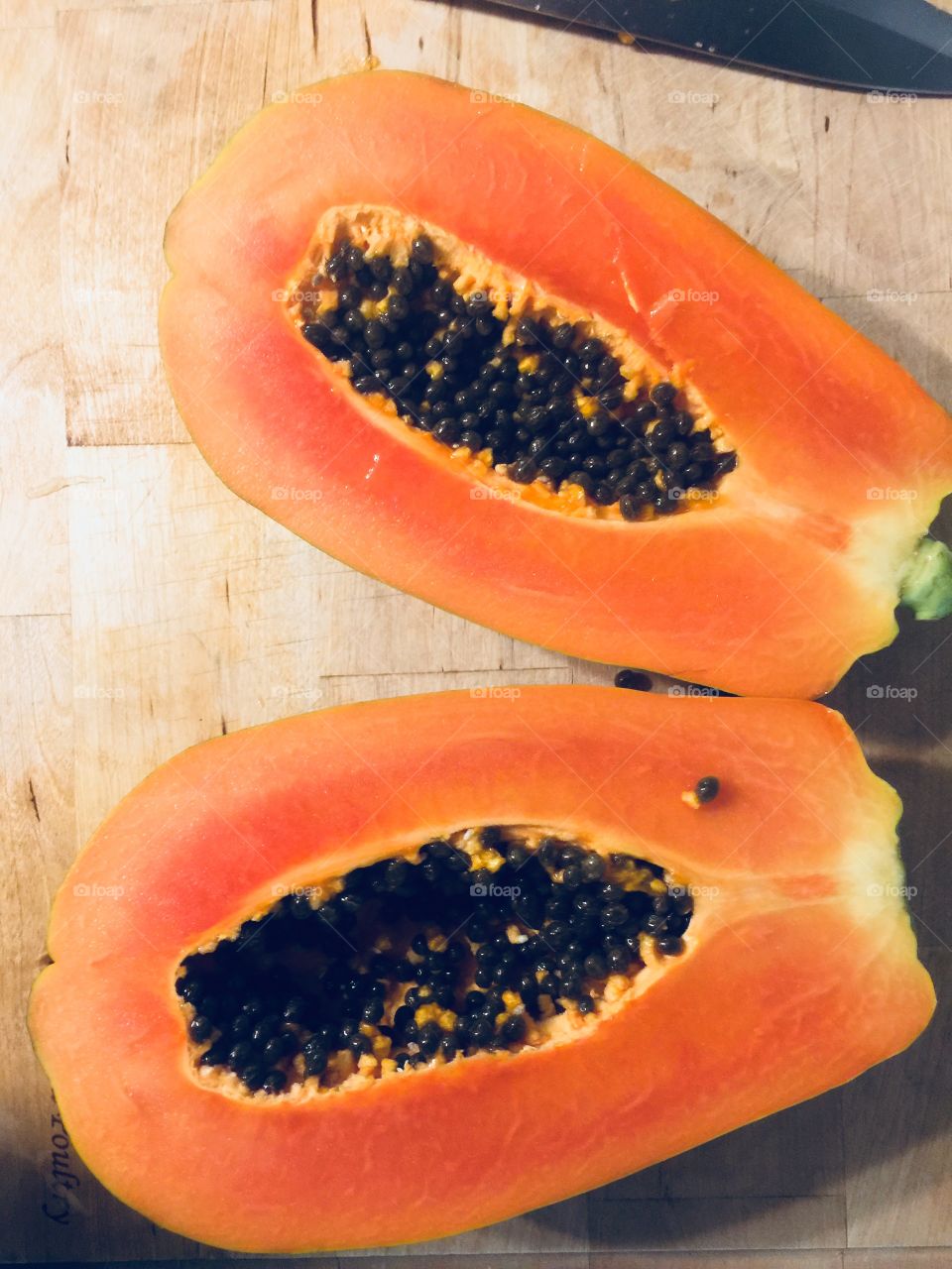 Mexican papaya cut in half. Seeds still inside the fruit. Both halves resting on a wooden surface.