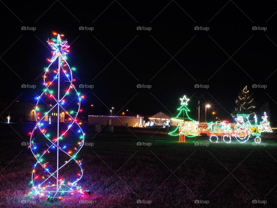 A beautiful outdoor Christmas light display shaped like a tree and a train driven by Santa lit up at night. 