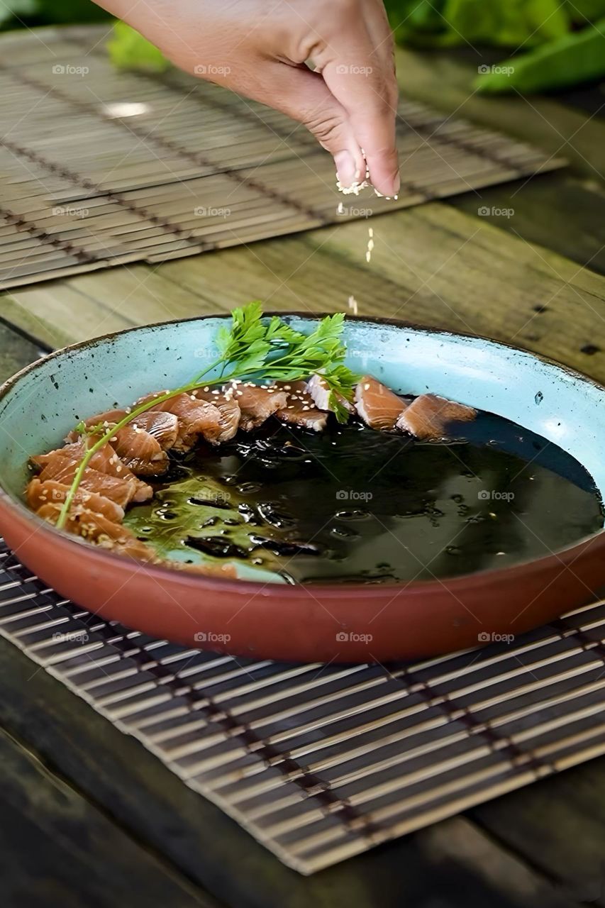 Sprinkling sesame seeds on a plate of tuna sushi