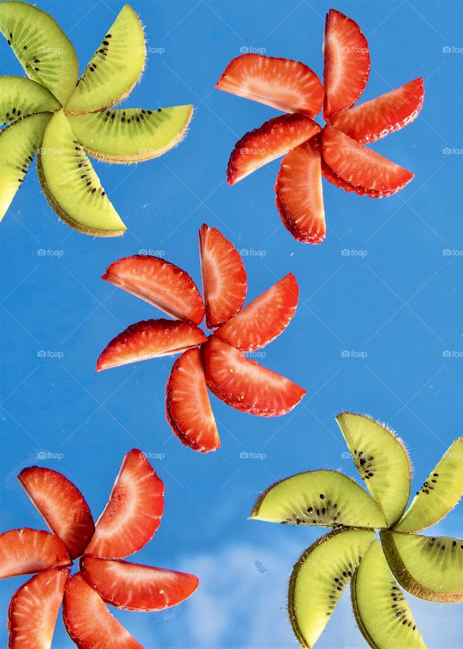 Kiwi and strawberry slices on a mirror with sky reflecting in the background 