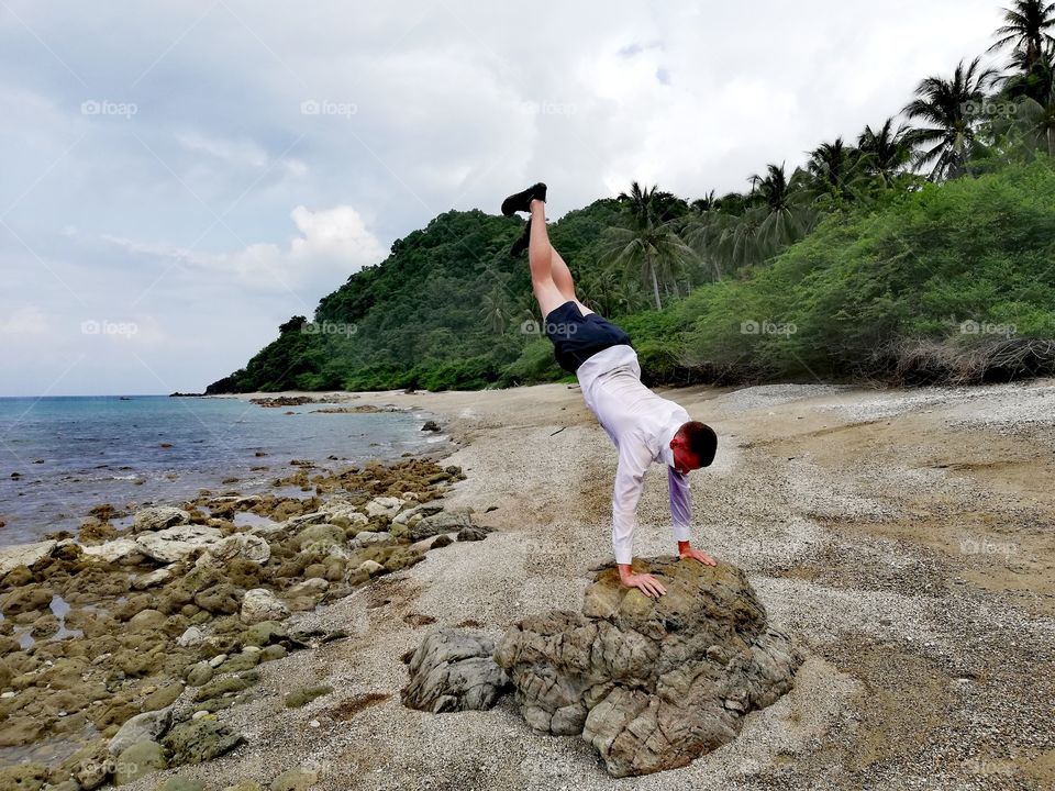 Sport at the beach, handstand on a rock on tropical beach in Mindoro, Island of Philippines