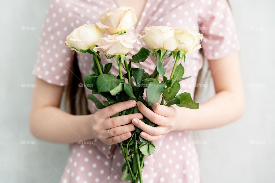 Pale pink dress. Young woman holds bouquet of white roses. Faceless portrait of young girl. Hands close up