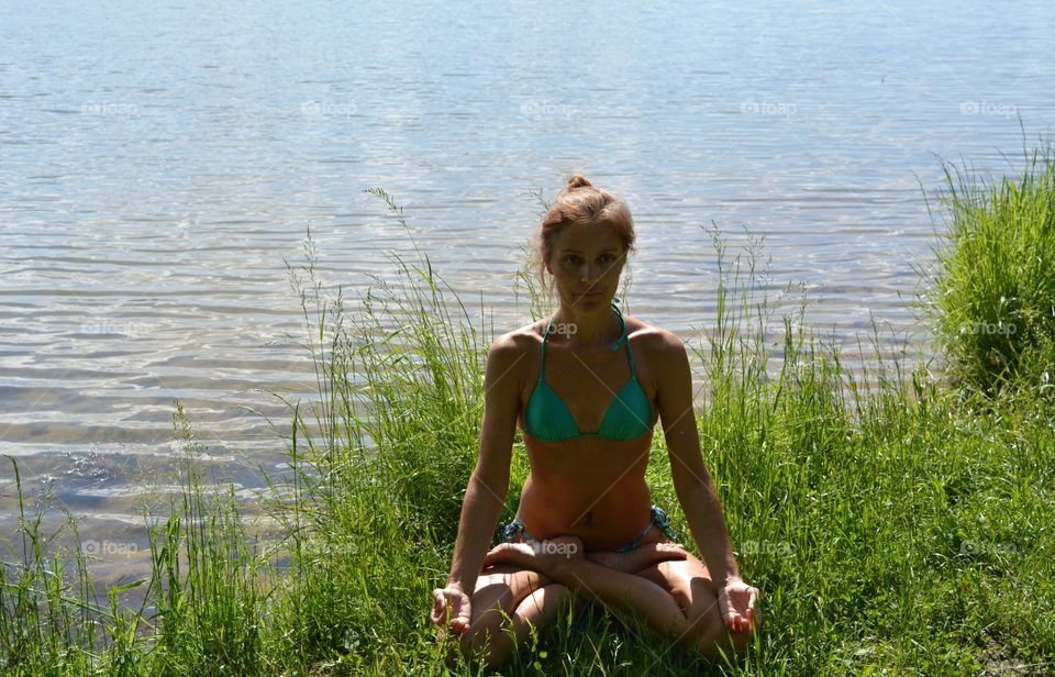 brunette girl in swimsuit training yoga lotus outdoor, summer time lake shore view