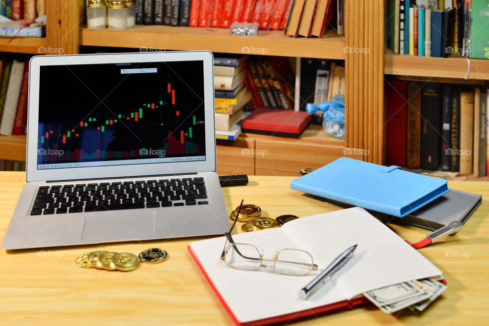 on the table golden cryptocurrency coins, notebook, pen, eyeglasses and laptop