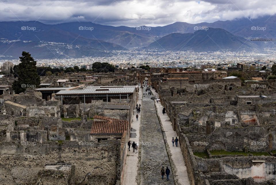 Beautiful view of the ruins of the ancient city of Pompeii in Italy with tourists walking along it against the backdrop of mountains with clouds on a gloomy day, close-up view from above.