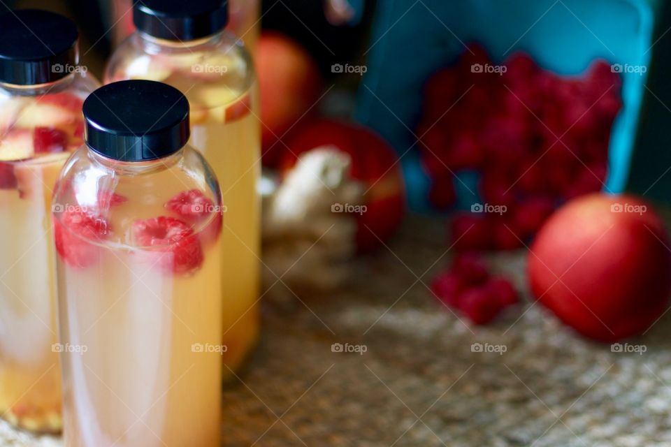 Kombucha, bottled for a second-ferment and flavored with nectarines, raspberries and slices of ginger root on a natural fiber mat, whole nectarines and raspberries in a paper carton in the background