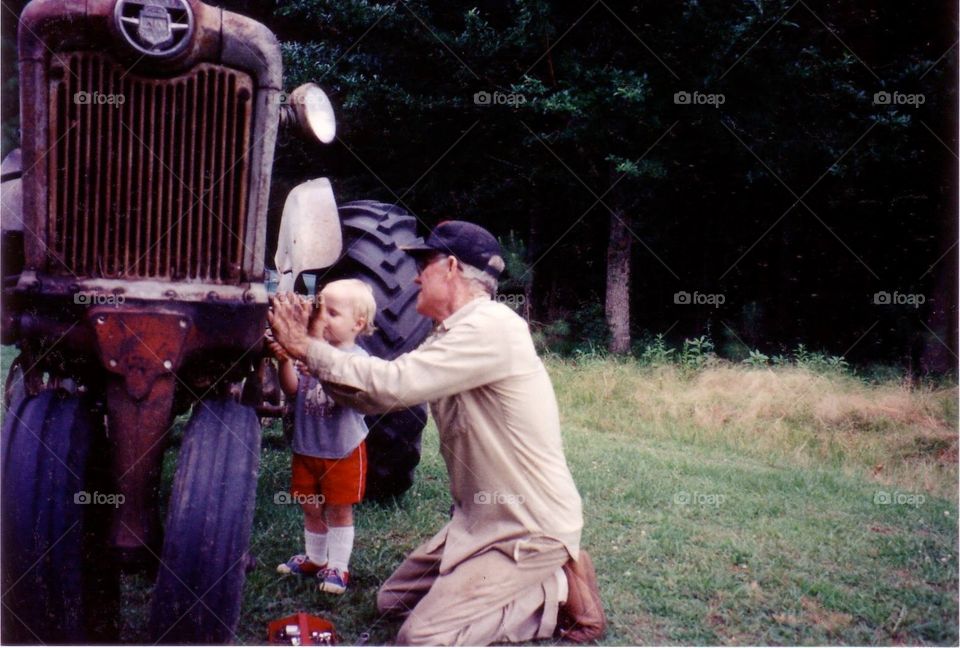 Young grandson helping grandpa work on tractor.